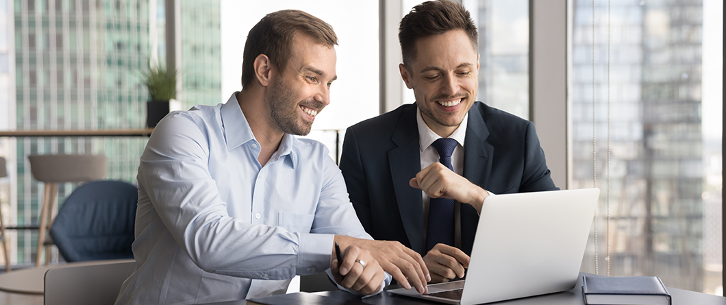 CrossSell and Product Penetration | Evok Advertising Two male coworkers in a bright office smile at a laptop about to fist bump in celebration of a collaboration