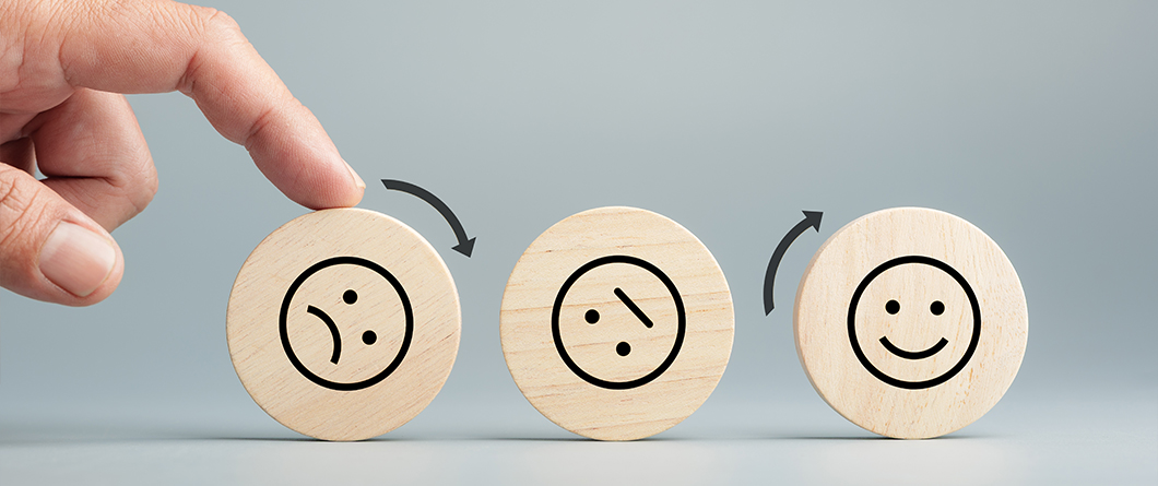 Managing Negative Reviews | Evok Advertising Three wooden discs with sad neutral and happy faces a hand rotates the left disc toward the middle with arrows showing the sequence