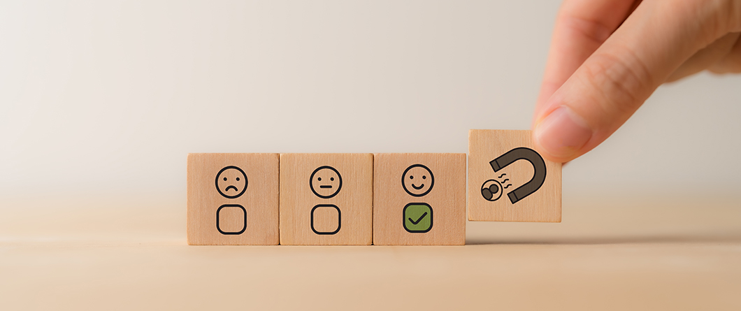 Measuring Retention Marketing | Evok Advertising Row of four wooden blocks with emoji faces representing satisfaction levels sad neutral happy green check and a hand placing a magnet icon block to symbolize attractionfeedback collection