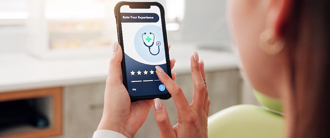 The Patient Decision Journey | Evok Advertising Person holding a smartphone displaying a'Rate Your Experience' feedback screen with a star rating in a clinic setting.