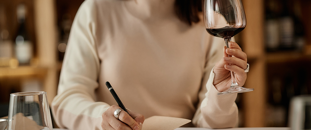 Crafting Messages That Convert | Evok Advertising Woman writing on a napkin at a table while holding a glass of red wine in a restaurant or wine bar nearby