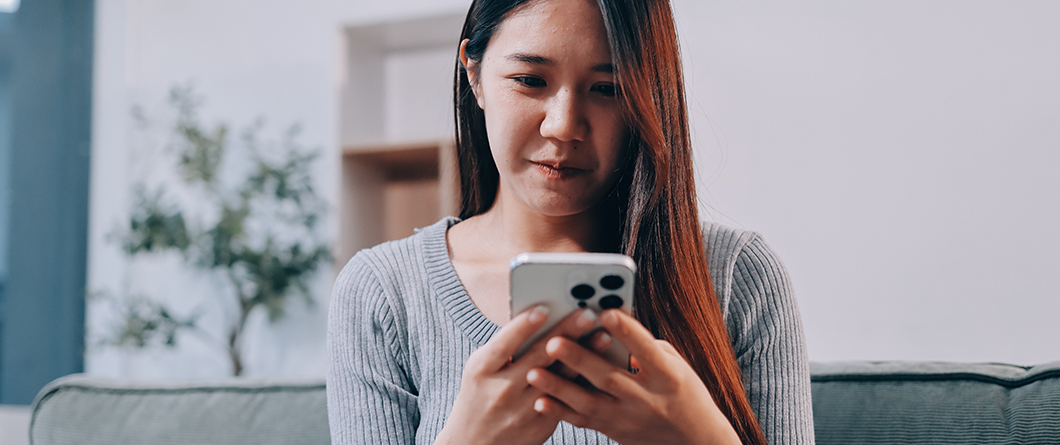 Measuring Engagement Marketing Performance | Evok Advertising Woman with long hair in a gray sweater sits on a couch and looks at her smartphone indoors